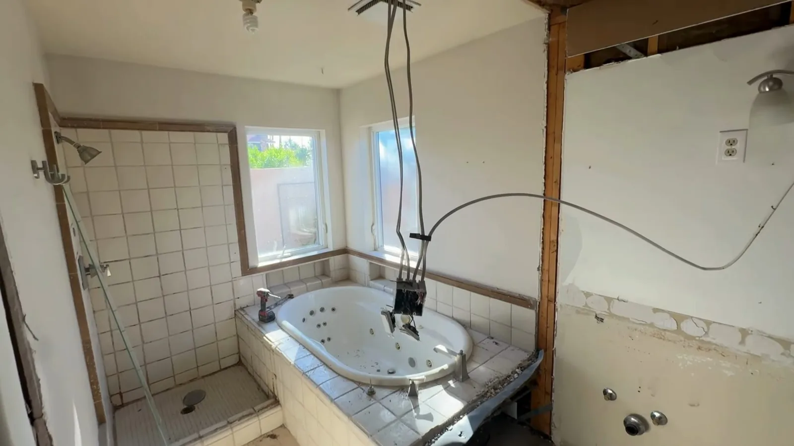 A bathroom with opened walls and ceiling, a tiled tub and cables hanging from above