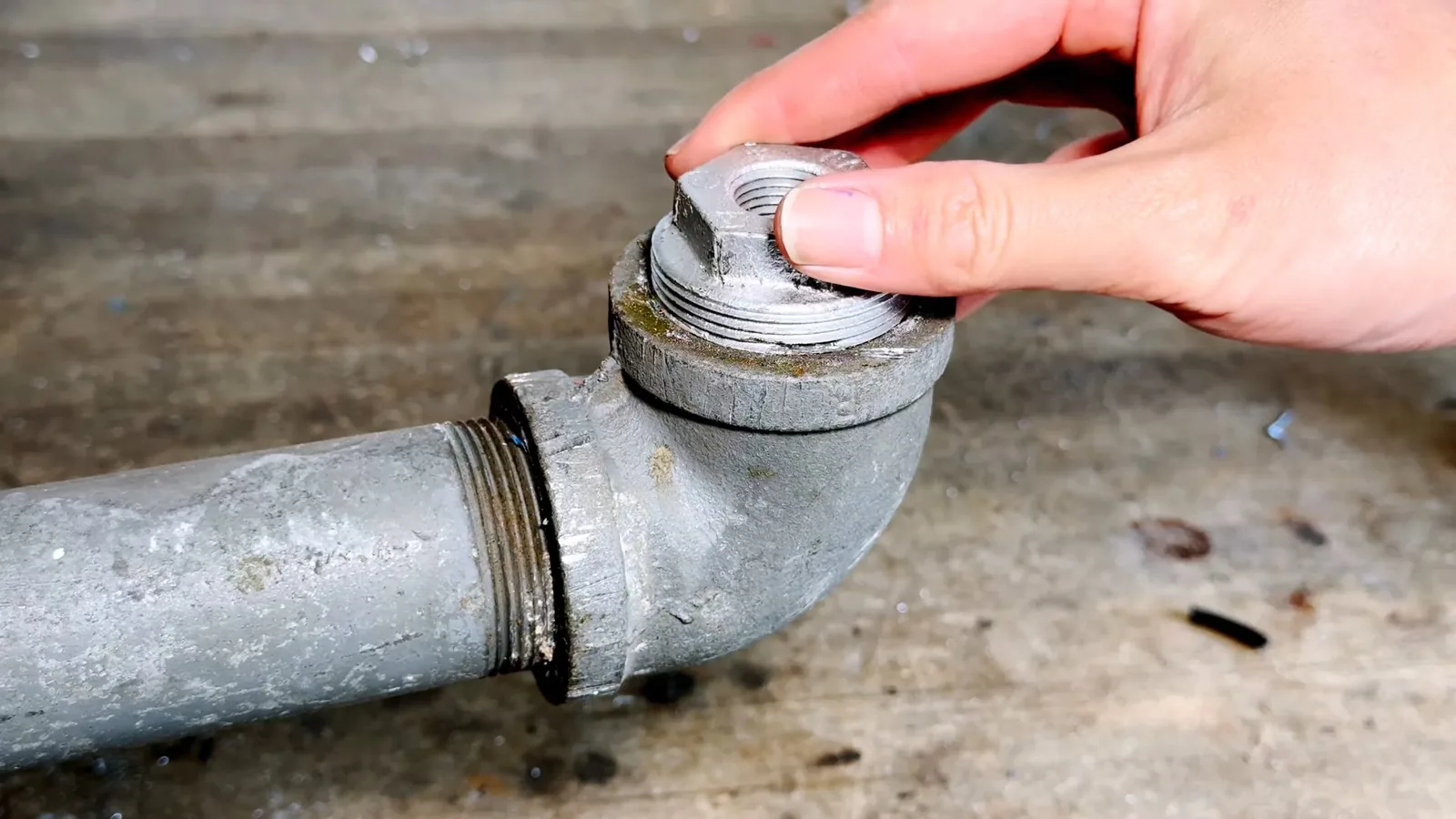 A hand unscrewing the threaded cap on a gray cleanout fitting