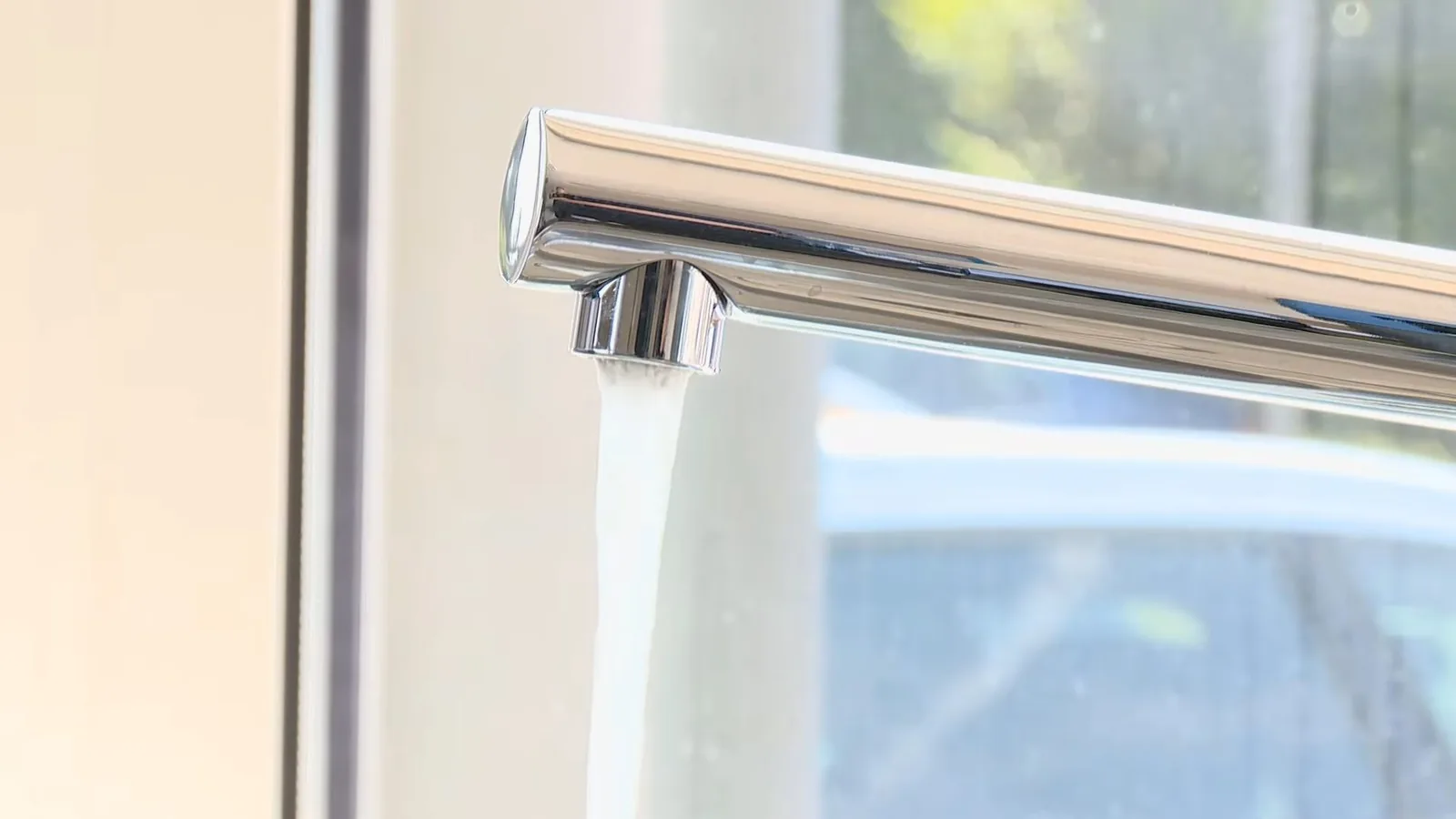A chrome kitchen faucet running a stream of water beside a bright window
