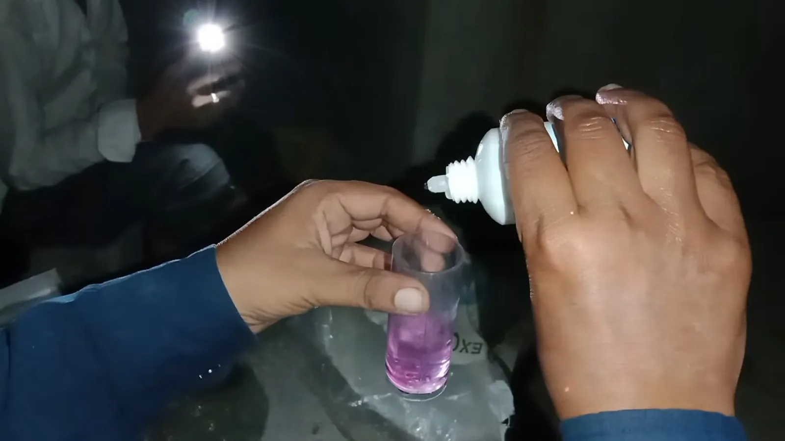 A hand adding drops from a small bottle to a glass holding pink liquid
