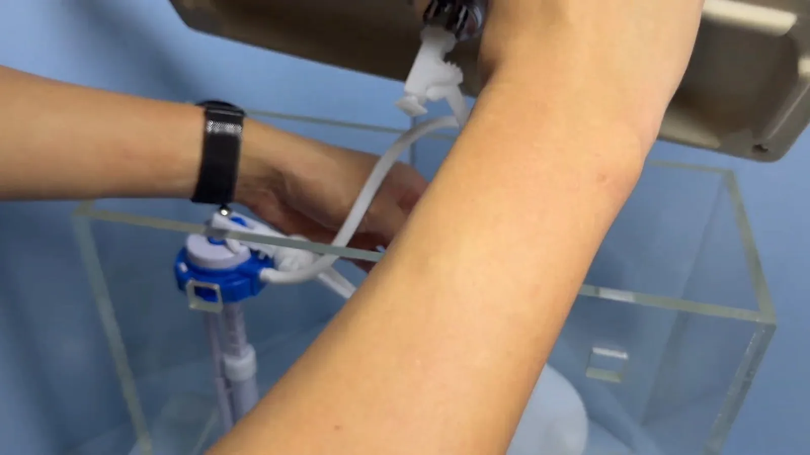 A hand adjusting the blue fill valve inside a clear toilet tank model