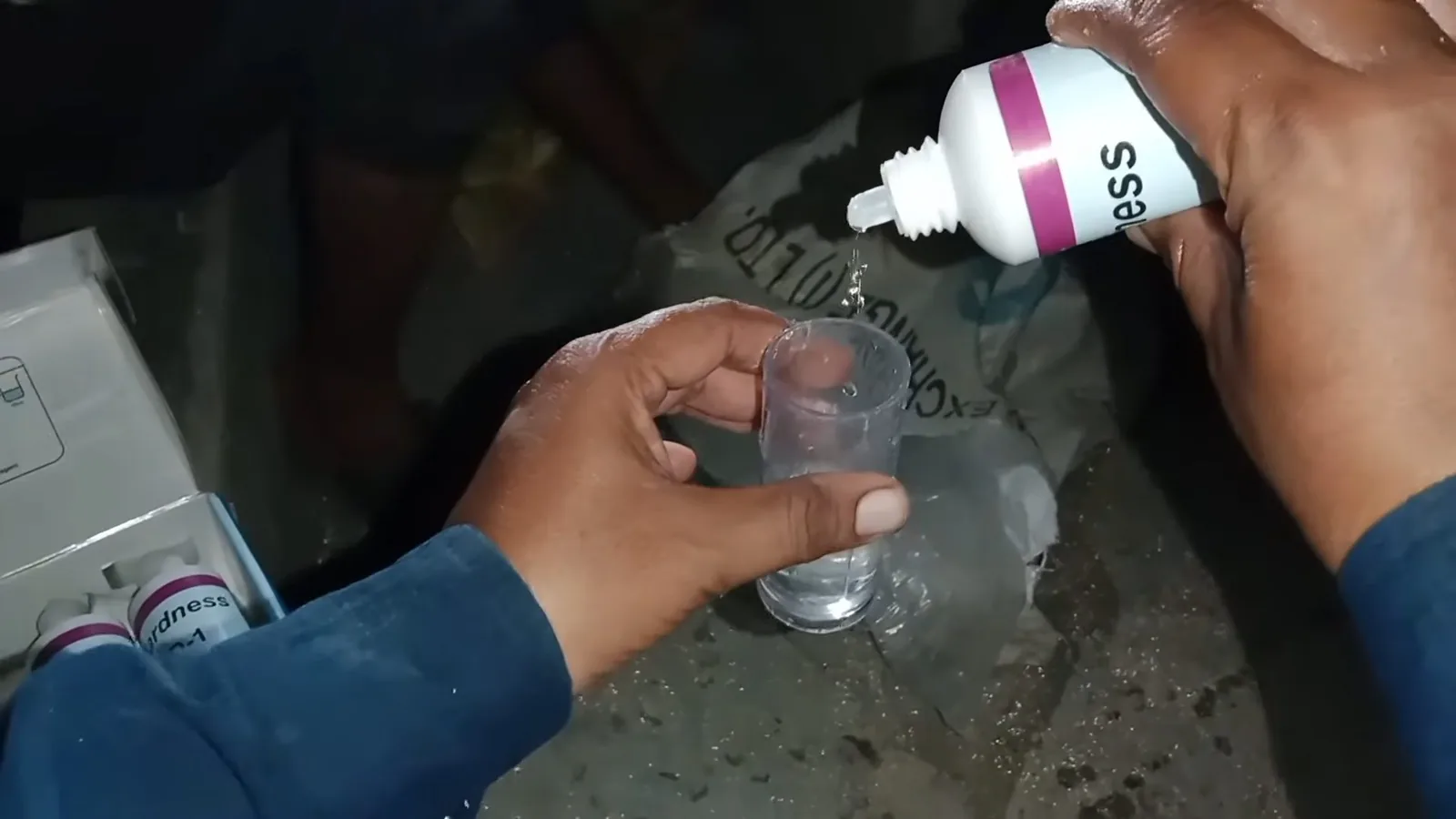 Hands holding a small glass while drops from a reagent bottle fall into the water