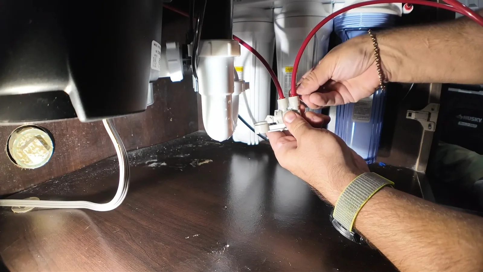 Two hands joining electrical wires on a unit mounted under a sink