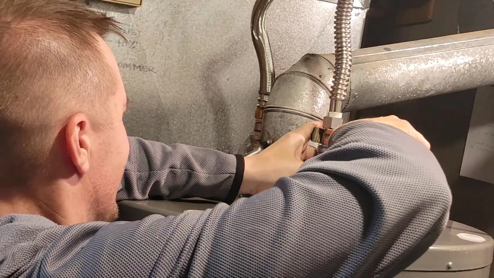 A man with short hair working on a pipe at the top of a water heater