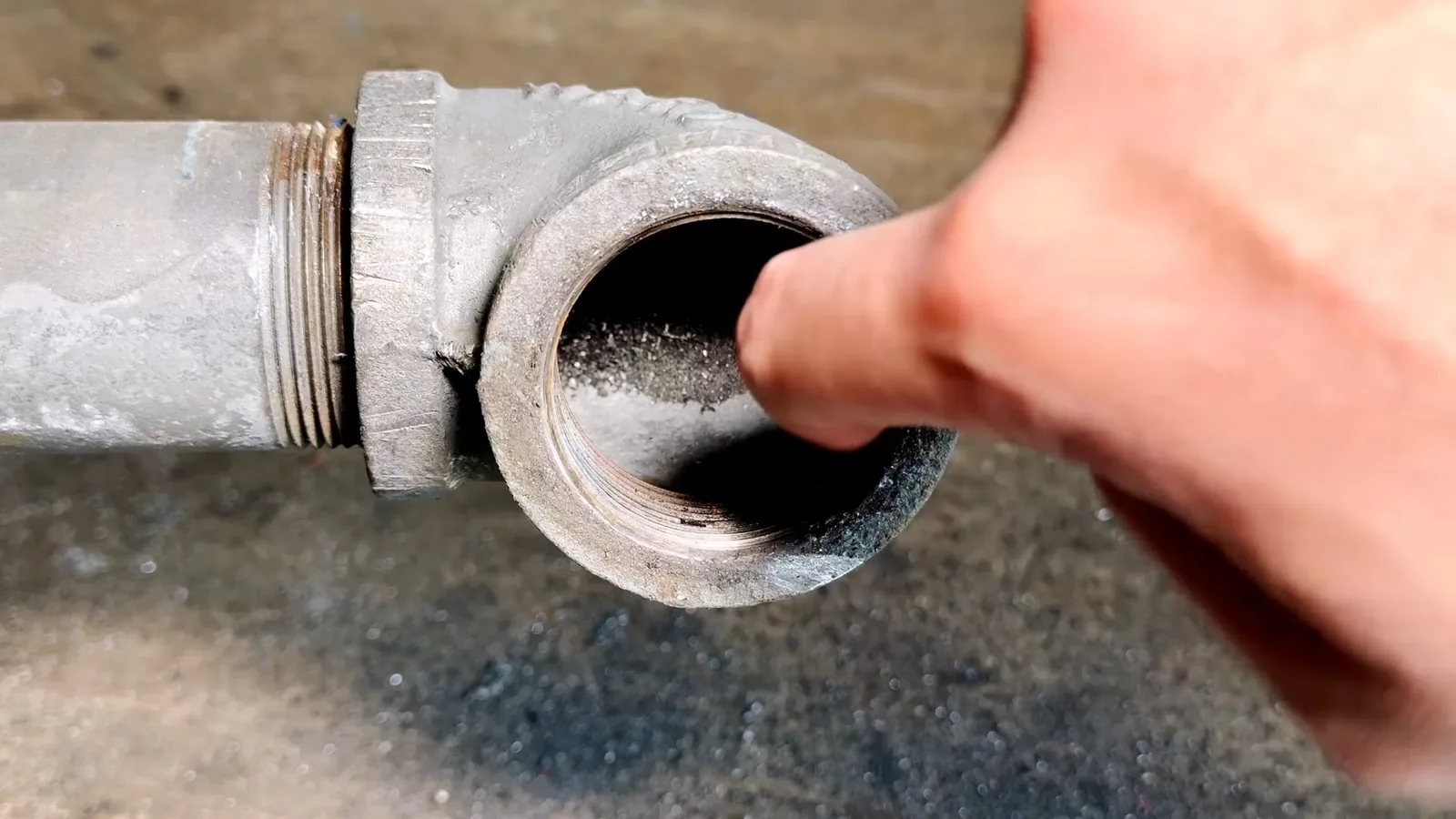 A fingertip at the open threaded end of a gray cast iron cleanout fitting