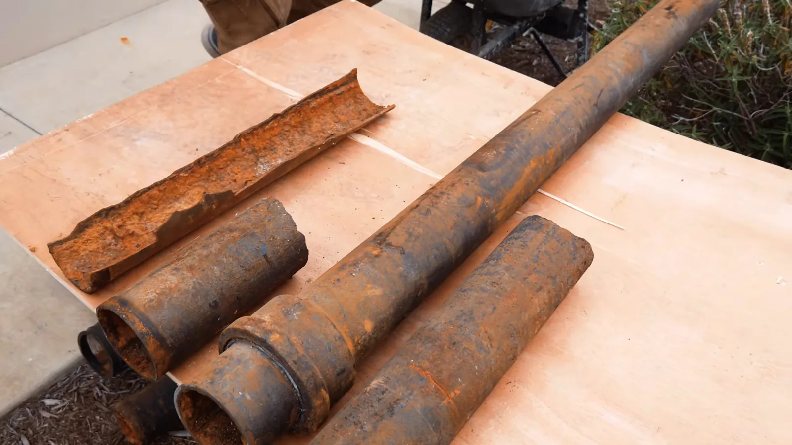Four sections of rust-covered cast iron pipe laid on a plywood sheet