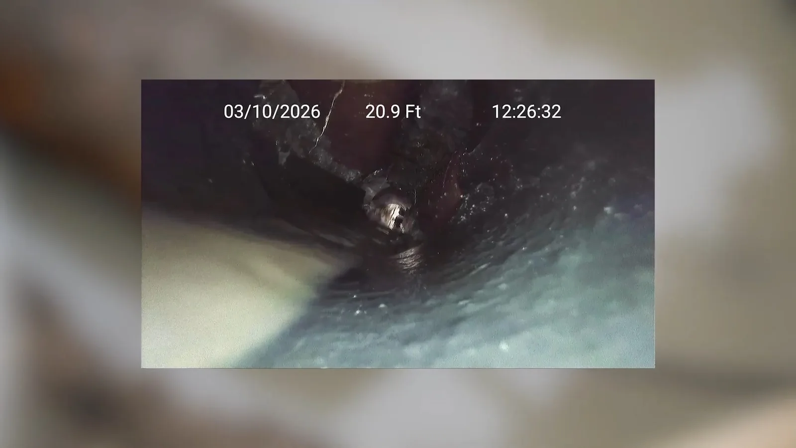 Sewer camera footage looking down a dark cast iron pipe, with a date and a distance reading in the frame