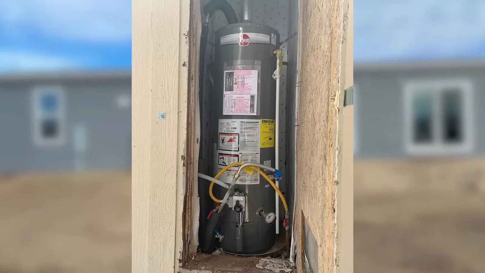 A tank water heater with warning labels standing in a narrow recess in a framed wall