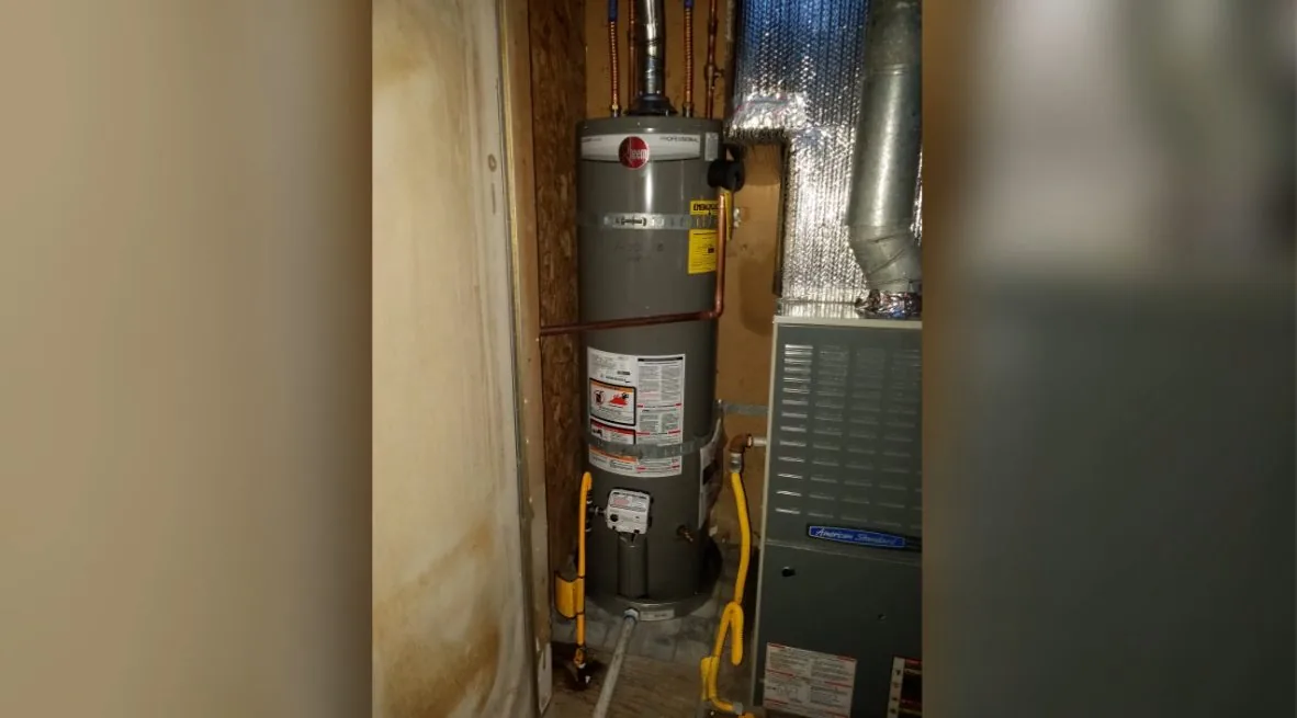 A tank water heater in a narrow closet beside a furnace