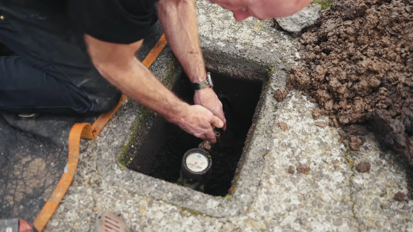 A technician kneeling at an open ground-level box and reaching in toward a water meter