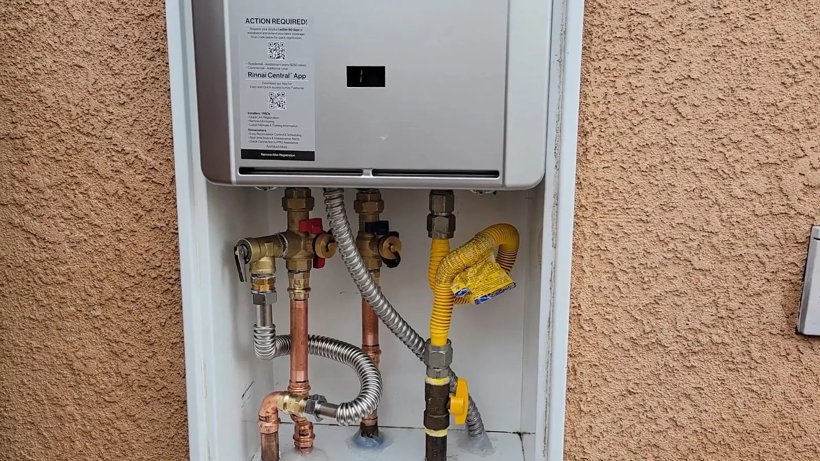 A wall-mounted tankless water heater in a recessed stucco niche with gas and water lines below it