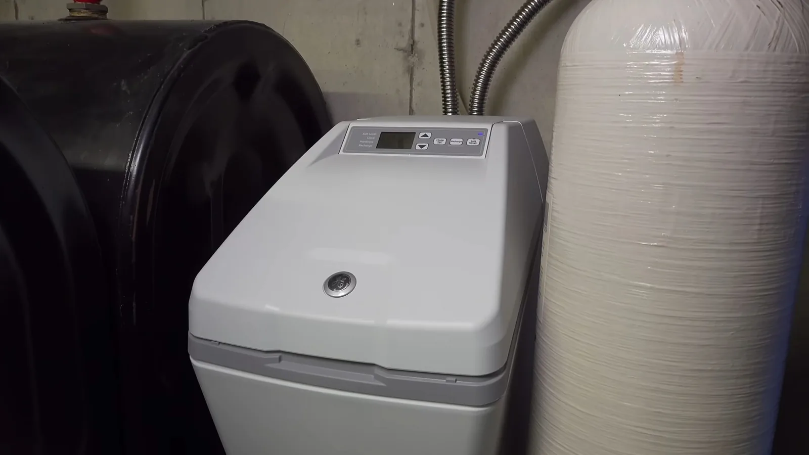 A gray water softener with a digital control head between a large black brine tank and a tall tan tank