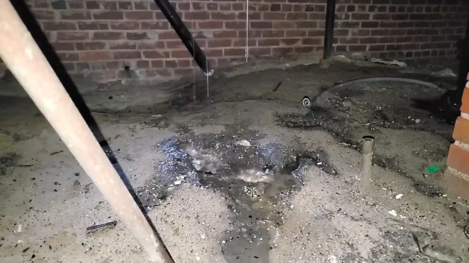 Wet ground and standing water beneath a pipe in a brick-walled crawlspace
